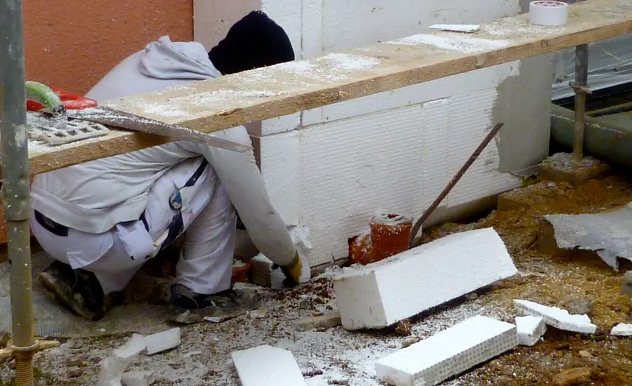 Handwerker bringt weiße Dämmplatten eines Wärmedämmverbundsystems am Sockel einer Hausfassade an