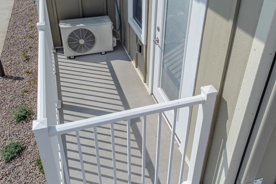 Weißes Außengerät einer Wärmepumpe auf einem Balkon neben einer Tür mit Jalousie, von oben fotografiert