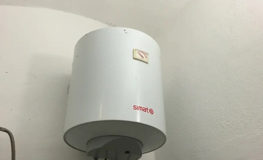 Weißer wandhängender Warmwasserspeicher mit Anschlussleitungen an einer verputzten Wand