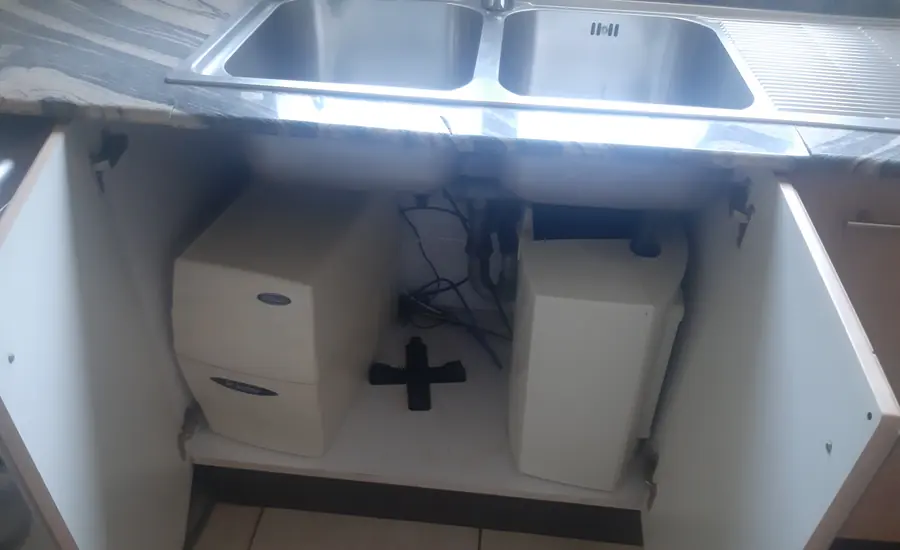 Zwei weiße Filtergehäuse einer Wasserfilteranlage im Unterschrank unter einer Spüle