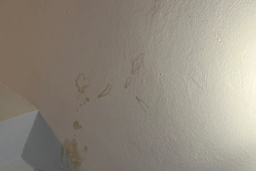 Gelbbraune Wasserflecken an einer verputzten Wohnungsdecke und Wand nach einem Wasserschaden