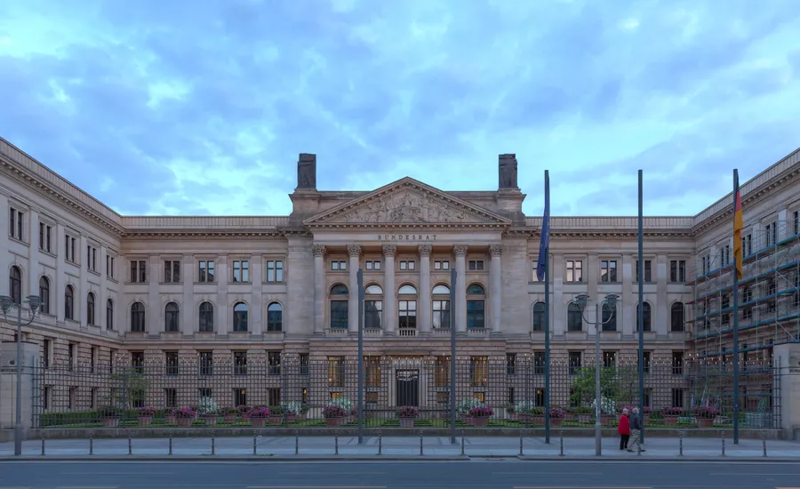 Hauptfassade des Bundesratsgebäudes an der Leipziger Straße in Berlin mit Säulenportal, Schriftzug „Bundesrat“, Fahnenmasten und Gitterzaun unter bewölktem Himmel