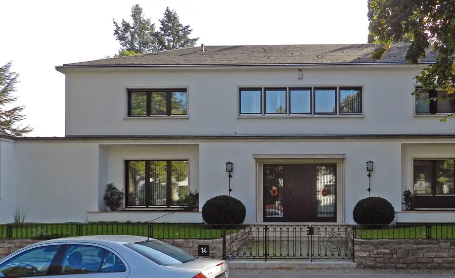 Weiß verputztes Wohnhaus mit dunklen Fenstern und Vorgarten