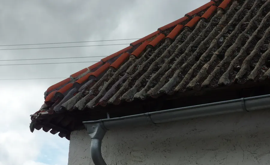Traufe eines Ziegeldachs mit Dachrinne und Regenfallrohr am Gebäuderand